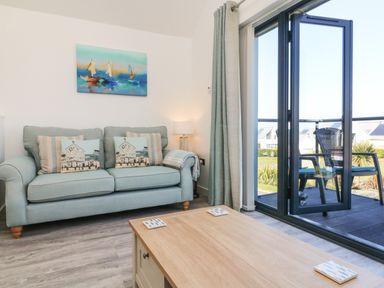 A living room with a light blue sofa and cushions a wooden coffee table and a glass door leading to a balcony with chairs at Seaquel in Westward Ho