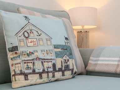 A cushion with a seaside building design on a sofa with a lamp in the background at Seaquel in Westward Ho