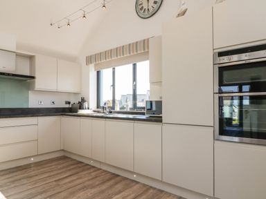 A kitchen with white cabinets a large window and built in oven at Seaquel in Westward Ho