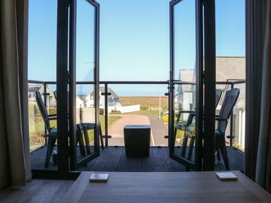 A balcony with two chairs and a small table overlooking houses and a road at Seaquel in Westward Ho
