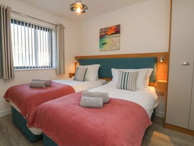 A bedroom with two single beds with red blankets rolled towels and striped pillows at Seaquel in Westward Ho
