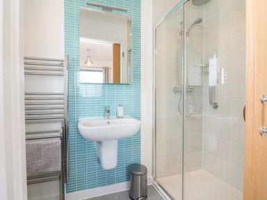A bathroom with a pedestal sink mirror towel rack and a glass shower enclosure at Seaquel in Westward Ho