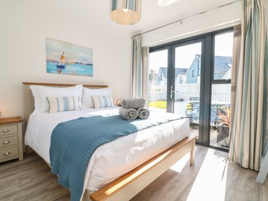 A bedroom with a bed with blue bedding beside a glass door leading outside at Seaquel in Westward Ho