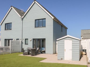 A backyard with a patio area containing a table and chairs a garden shed white fencing and a two-story house at Seaquel in Westward Ho