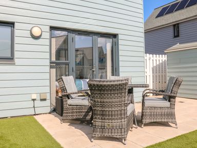 A patio with four wicker chairs around a table outside a light blue house at Seaquel in Westward Ho