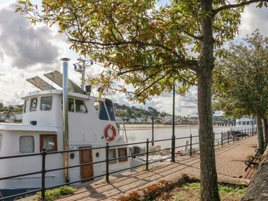 A riverside walkway with trees benches and moored boats at Seaquel in Westward Ho