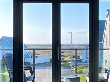 A view through glass doors of outdoor chairs a railing houses a street lamp and the sea beyond at Seaquel in Westward Ho