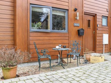 A small metal table with two metal chairs outside a wood-paneled house with a door and window at Maple in Falmouth