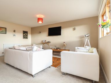 A living room with white sofas a wall-mounted television and a wooden coffee table at Maple in Falmouth