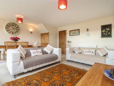 A living room with two sofas a wooden dining table with chairs a large wall clock and wall art at Maple in Falmouth