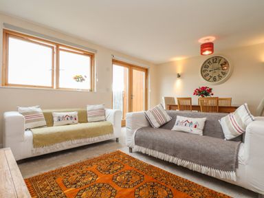 A living room with two sofas cushions a dining table and a large clock on the wall at Maple in Falmouth