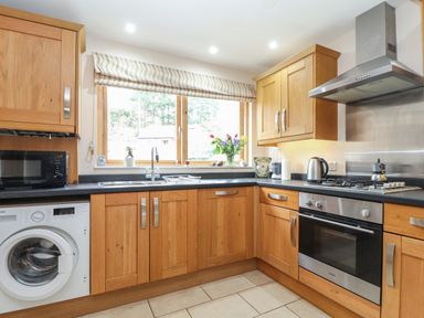 A kitchen with wooden cabinets a washing machine a microwave and a stove with a stainless steel hood at Maple in Falmouth