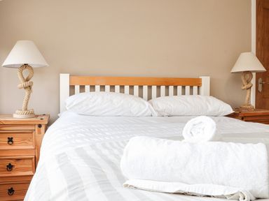 A bedroom with a bed featuring white pillows and linens with rolled towels on top and bedside tables with rope lamps at Maple in Falmouth