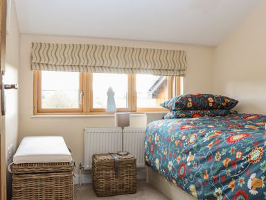 A small bedroom with a bed with floral bedding two wicker storage baskets and a window with a patterned blind at Maple in Falmouth