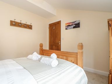 A bedroom with a wooden bed frame rolled towels on the bed a wooden door and a wall hook rack at Maple in Falmouth