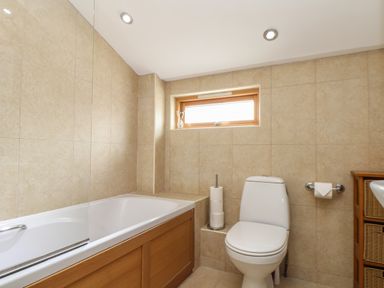 A bathroom with a bathtub a toilet a small window and a wooden cabinet at Maple in Falmouth