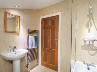 A bathroom with a wooden door a white pedestal sink a mirror towel rack with a striped towel and a bathtub with a shower at Maple in Falmouth