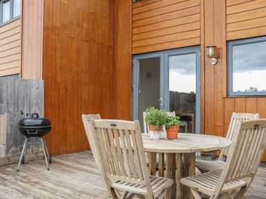 A wooden outdoor deck with a round table and four chairs and a barbecue grill at Maple in Falmouth