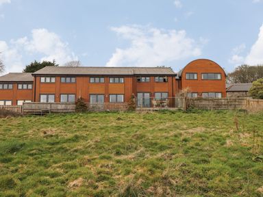 A large wooden building with many windows and a fenced grassy area in front at Maple in Falmouth