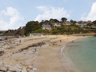 A sandy beach with people near the water and a hillside with houses in the background at Maple in Falmouth