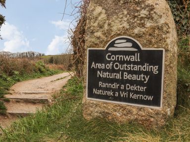 A stone sign marking Cornwall Area of Outstanding Natural Beauty on a dirt path with grassy surroundings