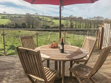 An outdoor wooden table with four chairs on a deck with a wine bottle two wine glasses and a fruit basket with an umbrella and countryside view at Maple in Falmouth
