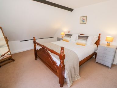 A bedroom with a wooden bed a standing mirror and bedside tables with lamps at Manor Farm Cottage in Hill Croome near Upton Upon Severn