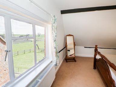 A bedroom with a wooden bed frame a standing mirror and a window showing a grassy field at Manor Farm Cottage in Hill Croome near Upton Upon Severn