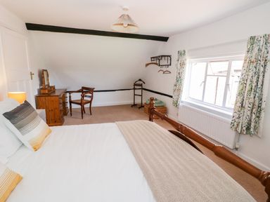 A bedroom with a wooden bed desk chair window and floral curtains at Manor Farm Cottage in Hill Croome near Upton Upon Severn