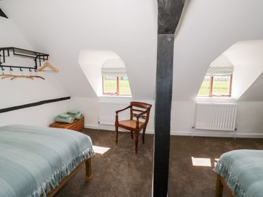 A bedroom with two single beds folded towels on a crate a wooden chair and two windows at Manor Farm Cottage in Hill Croome near Upton Upon Severn