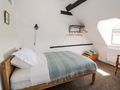 A bedroom with a single wooden bed with white sheets and a blue blanket and a window with folded green towels on a wooden crate at Manor Farm Cottage Hill Croome near Upton Upon Severn