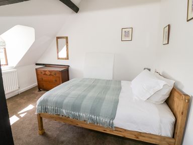 A bedroom with a wooden bed with white linens and a green throw a wooden chest of drawers and framed pictures on the walls at Manor Farm Cottage in Hill Croome near Upton Upon Severn