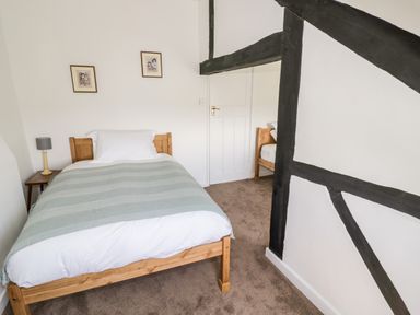 A bedroom with a wooden bed single bed with a side table and lamp and framed pictures on the wall at Manor Farm Cottage in Hill Croome near Upton Upon Severn