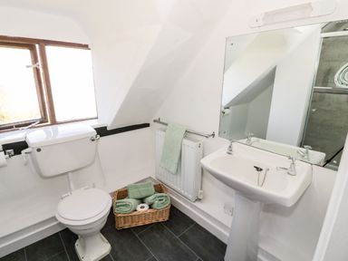 A bathroom with a toilet sink mirror towel rack and basket with towels at Manor Farm Cottage in Hill Croome near Upton Upon Severn