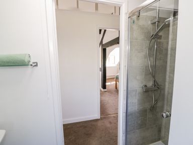 A bathroom with a glass shower, a green towel on a rack and a view into a carpeted room with wooden beams at Manor Farm Cottage in Hill Croome near Upton Upon Severn