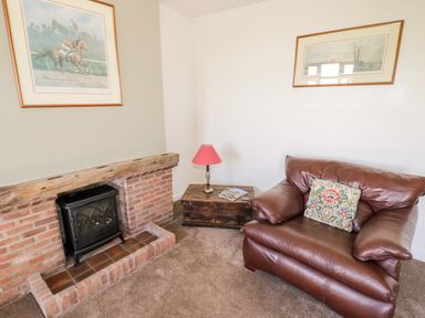 A room with a leather armchair and a brick fireplace with a wood stove at Manor Farm Cottage in Hill Croome near Upton Upon Severn
