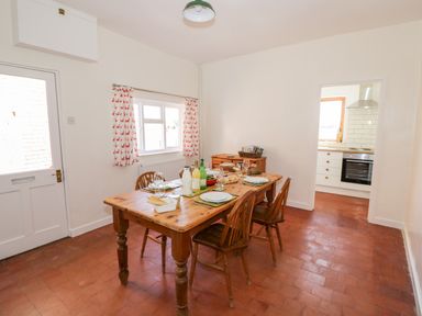 A dining room with a wooden table set for four and a view into a kitchen at Manor Farm Cottage in Hill Croome near Upton Upon Severn