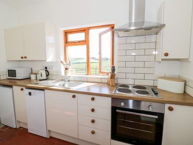 A kitchen with white cabinets a microwave kettle stove and oven with a window showing a green field at Manor Farm Cottage Hill Croome near Upton Upon Severn