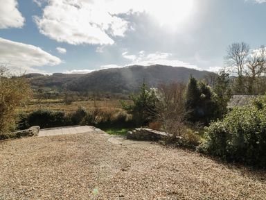 A gravel driveway with bushes and trees and hills in the background at The Old Smithy Cottage in Maentwrog near Penrhyndeudraeth