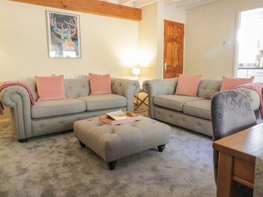 A living room with two grey sofas with pink cushions a grey ottoman and a wooden door at The Old Smithy Cottage Maentwrog near Penrhyndeudraeth