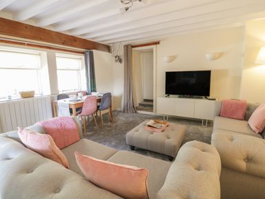 A living room with a TV on a white stand a dining table with chairs and couches with pink cushions at The Old Smithy Cottage in Maentwrog near Penrhyndeudraeth