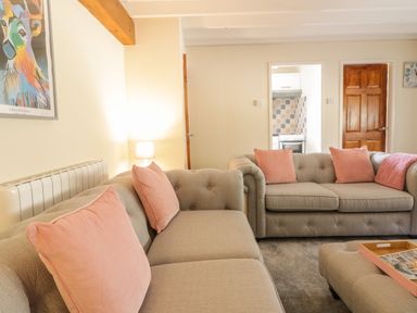 A living room with two beige sofas with pink cushions a lamp and a colorful dog painting at The Old Smithy Cottage in Maentwrog near Penrhyndeudraeth