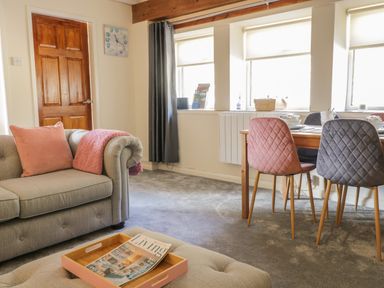 A living room with a grey sofa pink cushions and a wooden dining table with pink and grey chairs at The Old Smithy Cottage in Maentwrog near Penrhyndeudraeth
