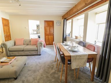 A living room with a sofa, dining table with chairs, and windows at The Old Smithy Cottage Maentwrog near Penrhyndeudraeth