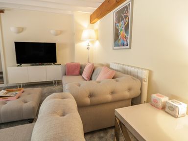 A living room with a sofa and ottoman near a television and a lamp at The Old Smithy Cottage in Maentwrog near Penrhyndeudraeth