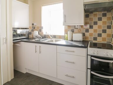 A kitchen with white cabinets a microwave kitchen sink toaster stovetop and tiled backsplash at The Old Smithy Cottage Maentwrog near Penrhyndeudraeth
