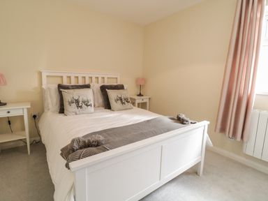 A bedroom with a white bed frame two cushions with deer images two bedside tables with lamps and pink curtains at The Old Smithy Cottage in Maentwrog near Penrhyndeudraeth