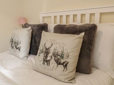 A bed with decorative pillows including deer print cushions and grey furry cushions at The Old Smithy Cottage Maentwrog near Penrhyndeudraeth