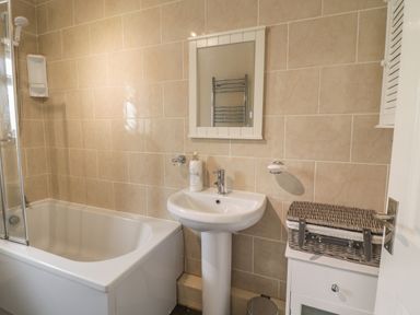 A bathroom with a bathtub shower basin wall mirror and cabinet with a wicker basket at The Old Smithy Cottage Maentwrog near Penrhyndeudraeth