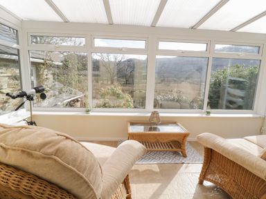 A sunroom with wicker furniture and a telescope by large windows at The Old Smithy Cottage in Maentwrog near Penrhyndeudraeth
